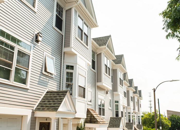 Row of modern townhouses with gray siding and white trim, nestled in charming east Tennessee. Each boasts multiple floors, large windows, and gable roofs. Greenery accents the foreground alongside a streetlamp, offering an inviting view for those interested in realty.